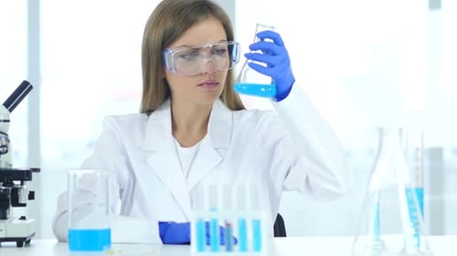 Woman Scientist Examining Flask With Blue Liquid