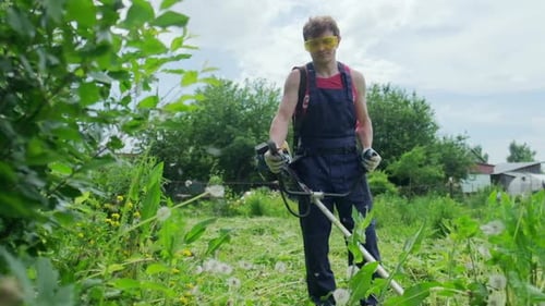 Worker and mower. Man uses a gasoline trimmer to mows a green grass in the garden