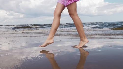 Young Woman with Long Legs is Walking Over Water in Summer Against the Sea with Many Waves