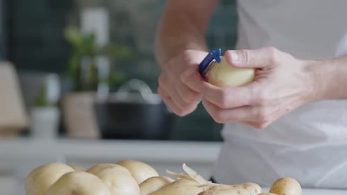Man Peeling Potatoes with Peeler in Bright Kitchen