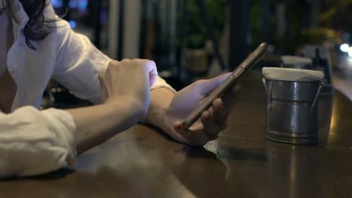 Woman Texting On Smartphone Sitting In Cafe At Night
