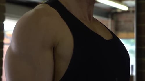 Muscly man in home gym exercising close up dumbbell shoulder raise