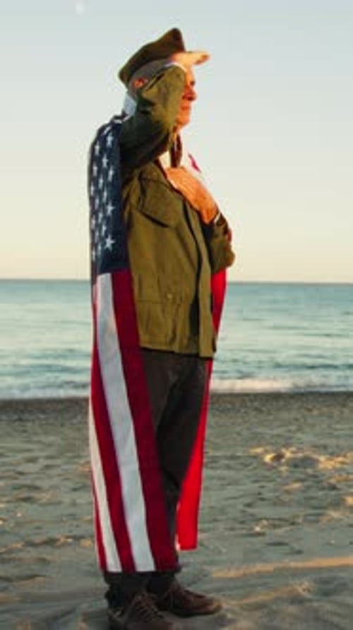 Senior Man Saluting with American Flag on Beach