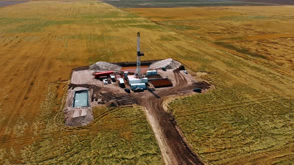 Oil rig in the vast field. High metal tower, pile of pipes, cars with ...