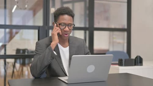 Young Adult Talking on Phone While Using Laptop