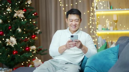Man Relaxing on Couch Using Smartphone at Christmas