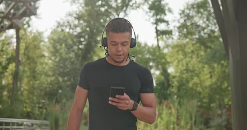 Man Walking with Phone and Headphones in Park
