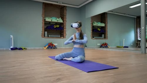 Woman in VR Glasses Sits in Lotus Pose on Blue Mat in Studio