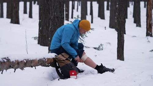 Hiker Bandaging Leg After Injury in Snowy Forest