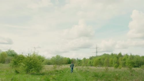 Man Walking Through Grassy Meadow on Sunny Day