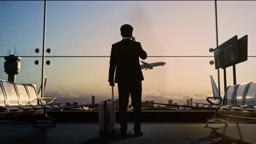Asian Businessman With Suitcase Talks On Smartphone In Waiting Room At Airport