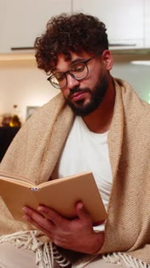 Man with Blanket Reading Book Indoors