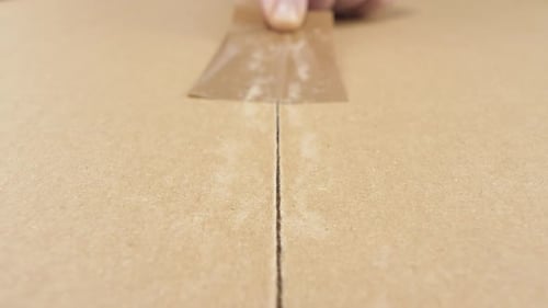 Hand Applying Tape to Brown Cardboard Box