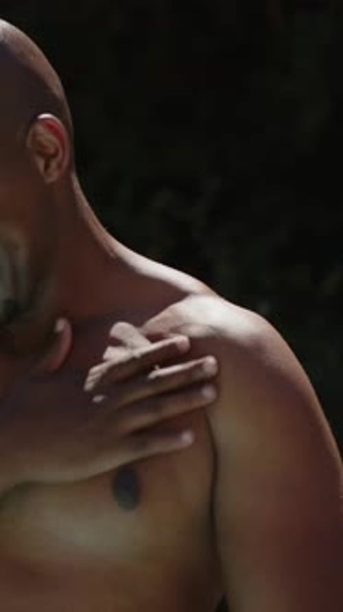 Vertical video: Laughing man self-touching, settling on pool towel while camera moving down, shorts