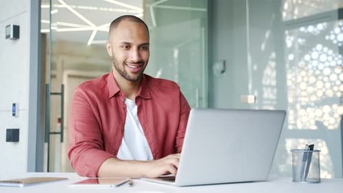 Smiling businessman working on a laptop while sitting at a workplace in a modern business office.