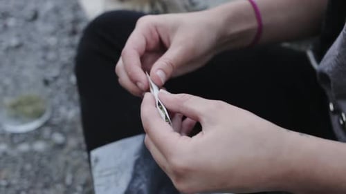 A young man is wrapping dried marijuana dried leaf in a small piece of paper - close up