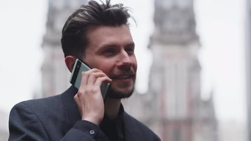 Handsome Young Businessman in Suit is Smiling While Talking on the Phone on Street