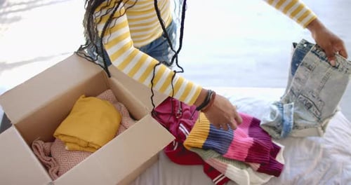 Packing clothes into cardboard box, woman organizing wardrobe at home