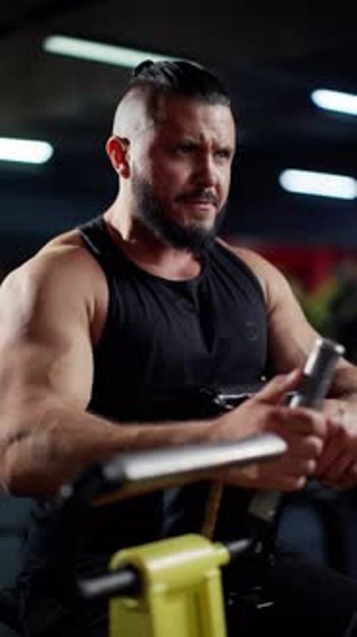 Muscular Man Intensely Working Out on a Rowing Machine in a Dark Gym