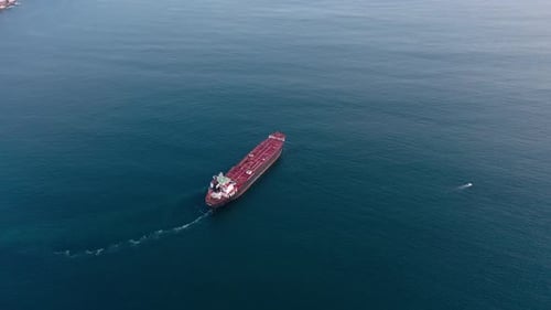 Luftflug über einem roten Frachtschiff auf ruhiger, blauer See bei Tag