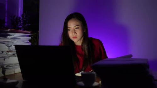 Asian woman working late at night with laptop computer home office looking screen monitor