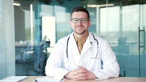 Smiling Doctor in White Coat Sitting at Desk