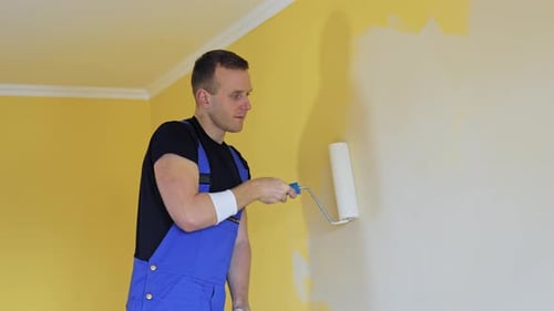 Professioneller Maler malt die Wände mit einer Walzenbürste. Arbeiter im blauen Overall
bei der Renovierung