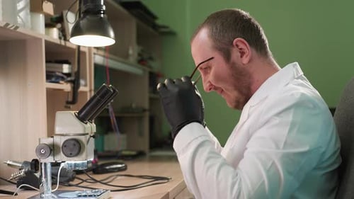 Man Examining Circuit Board Under Microscope in Lab