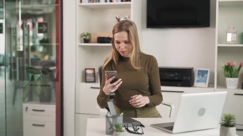 The young woman, blonde, works with a laptop in a modern, bright office. She receives a notification