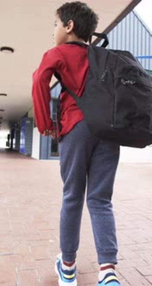 Vertical video: In school setting, young biracial student walks with black backpack