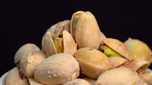 Salted pistachio nuts for beer background close up. Roasted pistachios rotate in a bowl on a black
