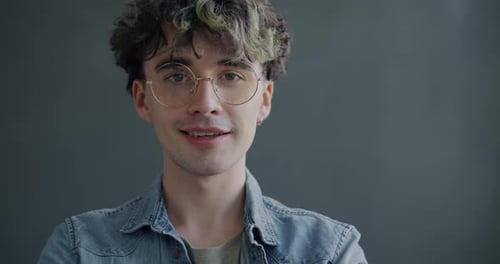 Portrait d'un jeune homme portant des lunettes à la mode souriant regardant la caméra sur fond de couleur grise