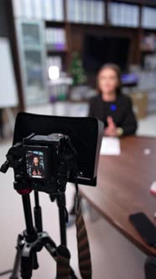 Professional camera with display filming a Caucasian brunette sitting at desk. Close up.