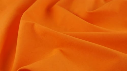 Top view of the soft folds of the squash orange cotton fabric. The textile background rotates
