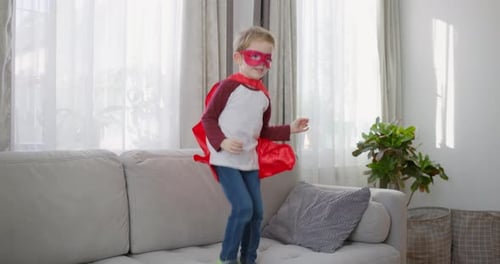 Enthusiastic Child Jumping on Couch in Superhero Costume