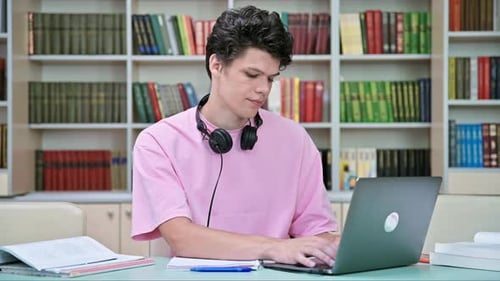 Young Male Student Sitting with Laptop with Books in College Library