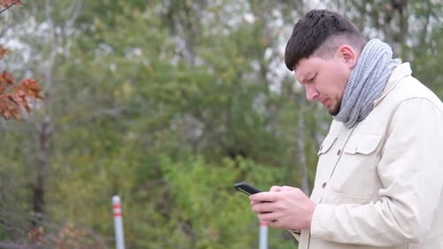 young caucasian man sitting on a bench in the park and using smartphone