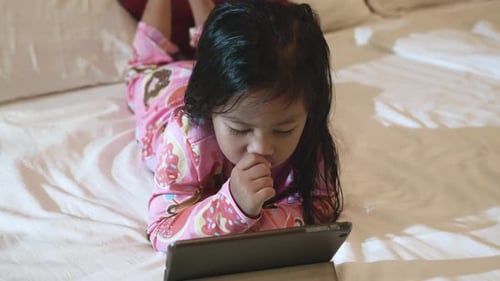 Child Lies on Bed Watching Tablet