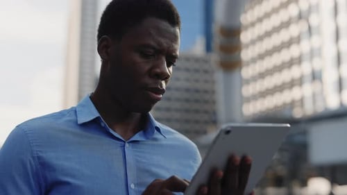 Junger afroamerikanischer gutaussehender, nachdenklicher Unternehmer, der mit digitalem Tablet aus der Ferne arbeitet