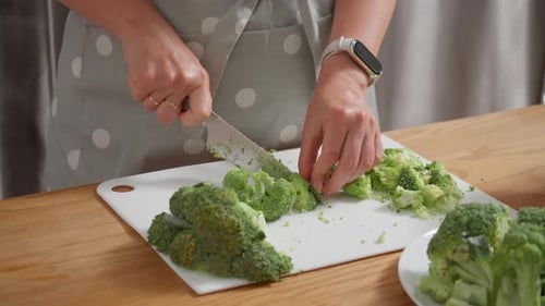 Woman's hands finely chopping fresh green broccoli on a white cutting board