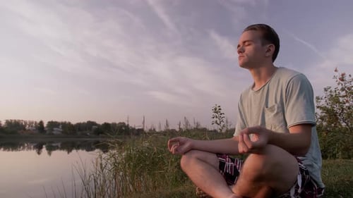Young Adult Meditating by Lake at Sunset