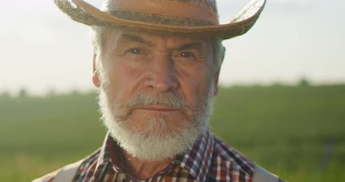 Portrait View of the Caucasian Professional Senior Happy Farmer Wearing Hat Standing in Backyard of