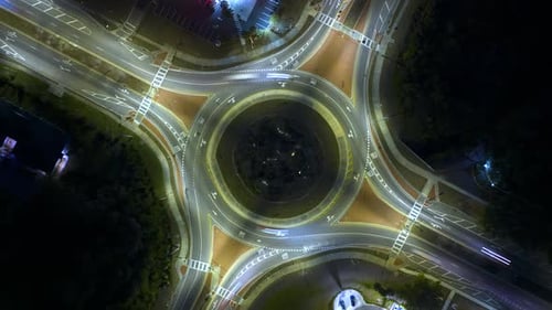 Blick von oben auf den Straßenverkehr der Stadt an der Kreisverkehrskreuzung bei Nacht mit schnell fahrenden Autos im Zeitraffer