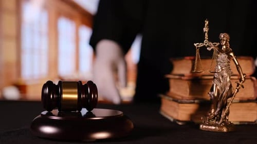 Hölzerner Hammer und bronzene Justizwaagen neben alten Gesetzesbüchern