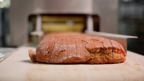 Bread on conveyor belt after long loaf cutting mechanism at factory close-up. Unrecognizable person