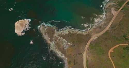 Mountainous landscape crossed by roads with moving cars. Sea-green water of Pacific ocean