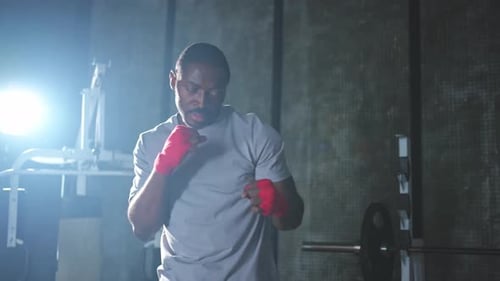 Fitness Workout in Gym African Man Fighter Preparing for Fight Punching with Red Boxing Wraps Sports