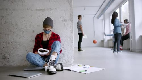 Un jeune étudiant portant un masque facial est assis sur le sol du couloir pendant la pandémie de coronavirus