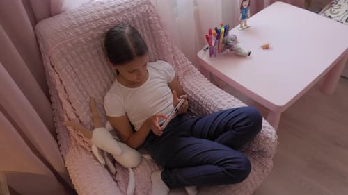 Girl Relaxing in Chair with Smartphone Indoors
