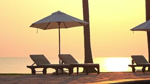 Close-up of empty beach loungers and sun umbrella at sunset.